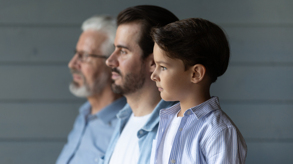 Close up side view of three generations of men stand in row look in distance show unity and family support - Small boy with young father and older grandfather